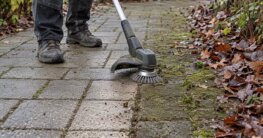 Rasentrimmer mit Unkrautbürste reinigt moosige Pflasterfugen im Herbst